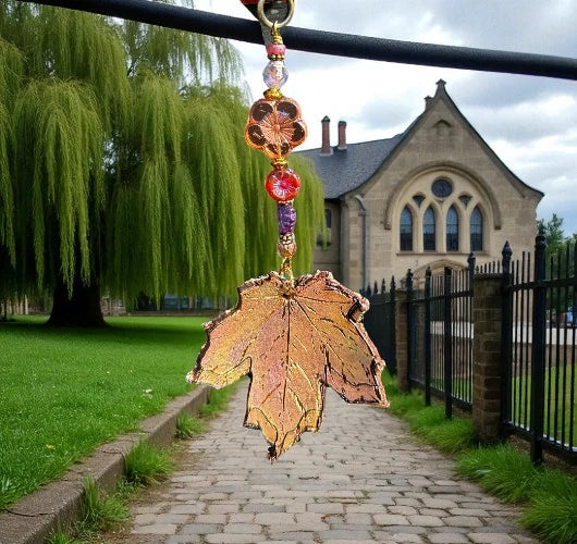 Decorative leaf ornament with beads hanging from a railing in a park.