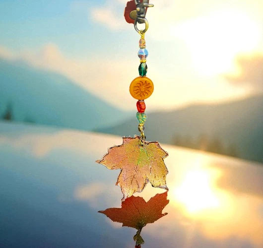 Decorative keychain with a leaf charm and beads against a blurred natural background