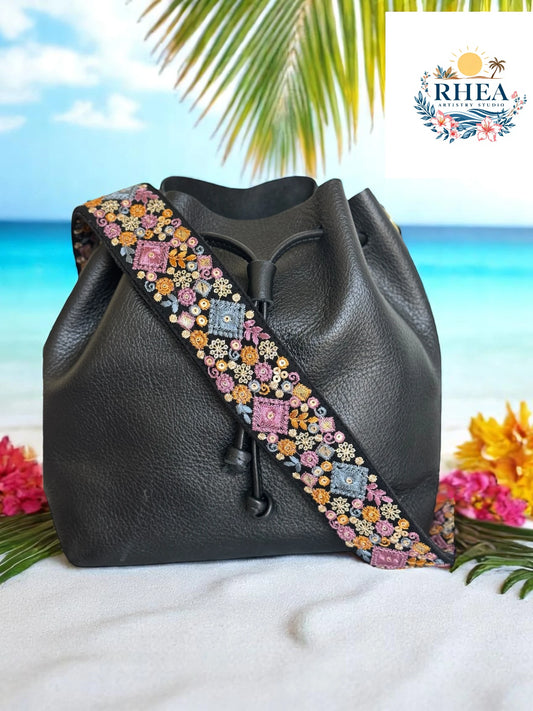 2-inch strap with bold embroidered lavender, gold, and blue squares surrounded by florals on a black base, styled with a black leather bag."