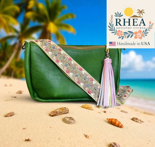 Green handbag with floral purse strap and tassel on a beach, featuring RHEA Artistry Studio logo.