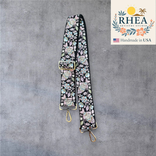 Floral patterned purse strap with gold hardware on a gray background, featuring RHEA Artists Studio logo.