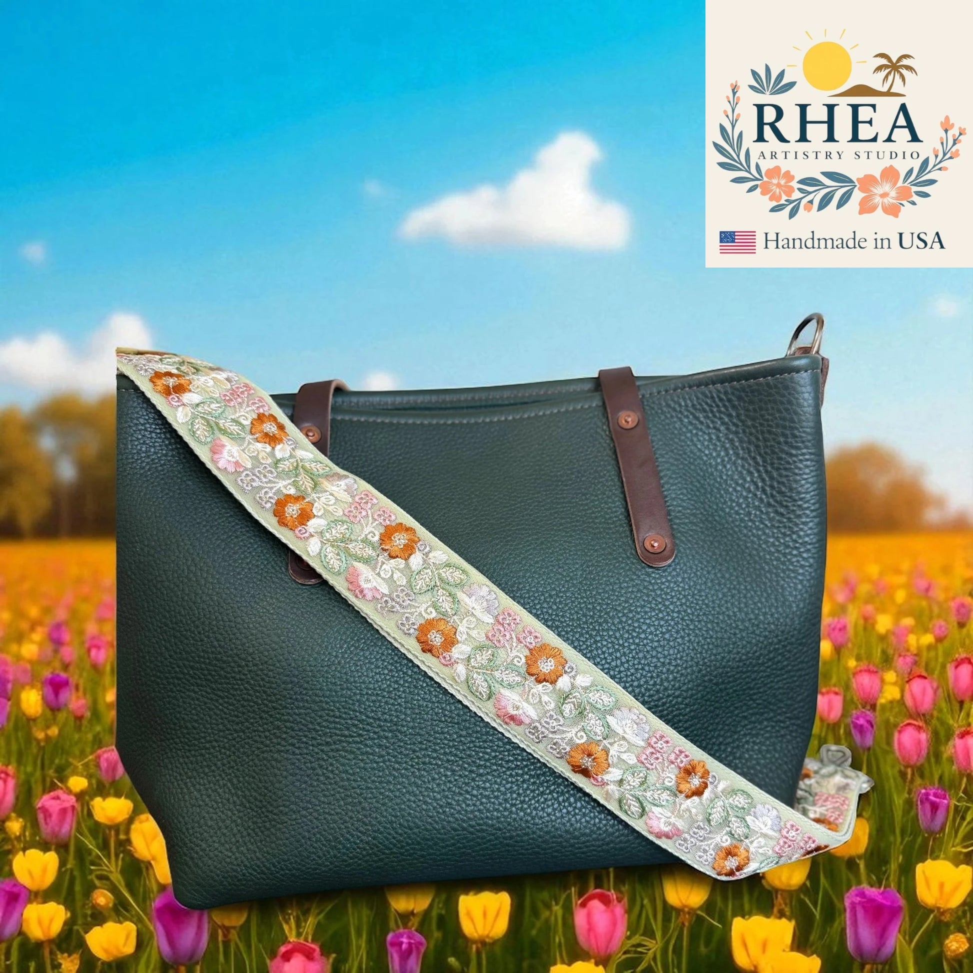 Green handbag with floral strap in a field of flowers, featuring RHEA Artistry Studio logo.