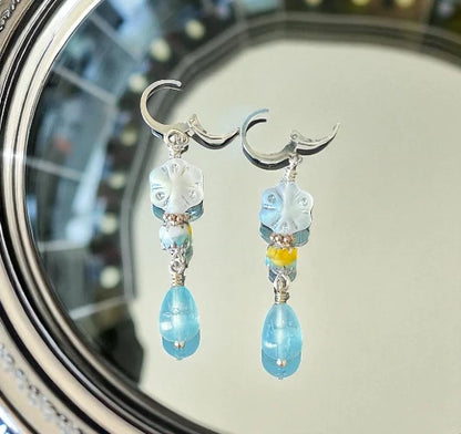 Pair of earrings with blue and clear beads on a reflective surface