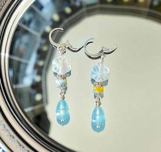 Pair of earrings with blue and clear beads on a reflective surface