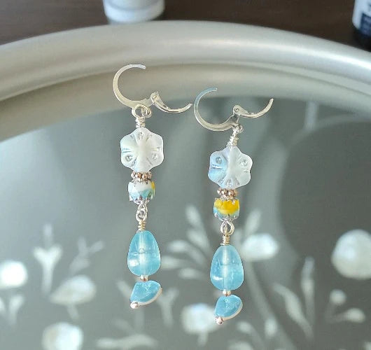 Pair of earrings with blue and clear beads on a reflective surface