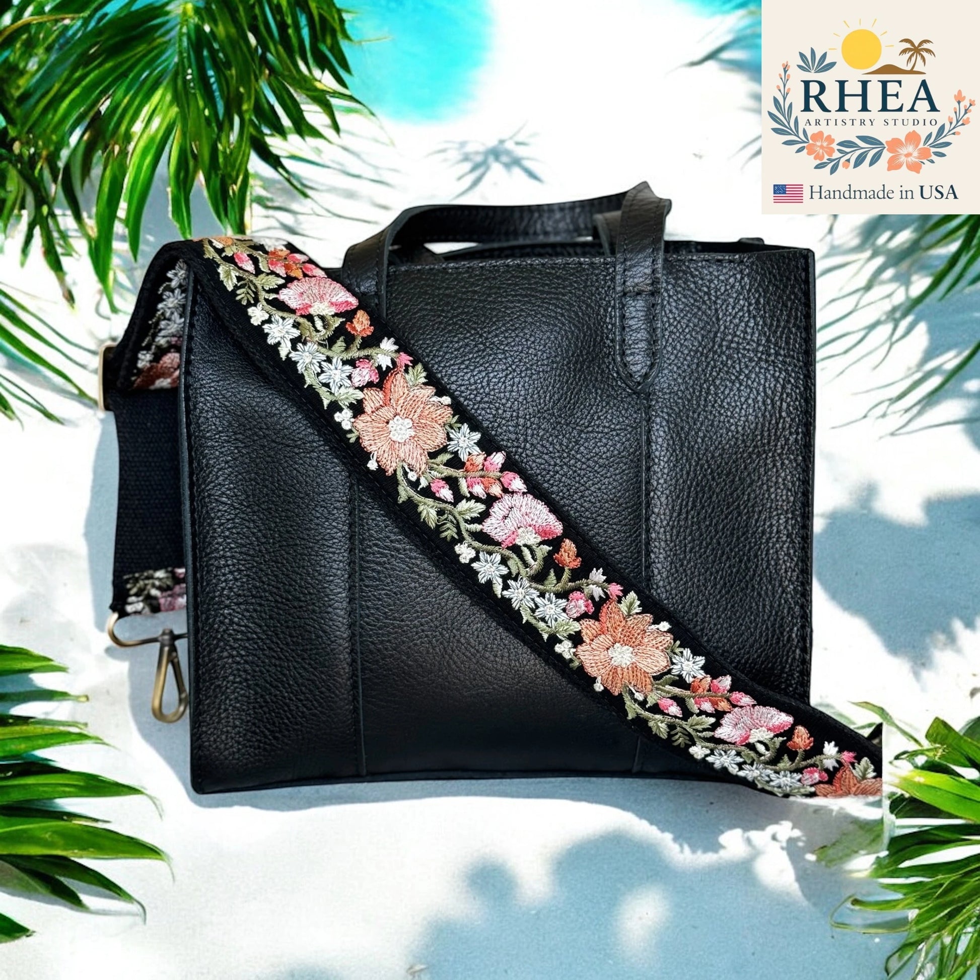 Black leather handbag with floral embroidery purse strap on a white background with palm leaves.