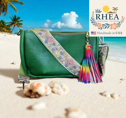 Green handbag with colorful tassel and purse strap on a beach, featuring RHEA Artistry Studio logo.