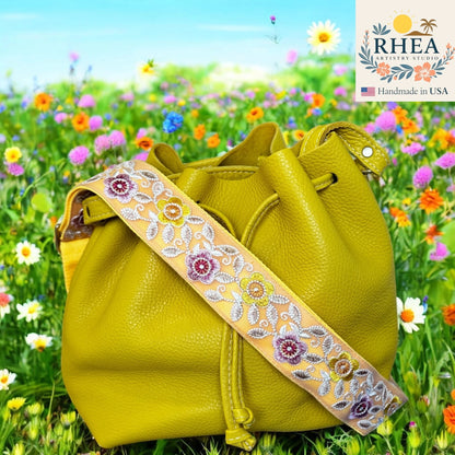 Yellow leather handbag with floral purse strap in a field of flowers, featuring the RHEA brand.