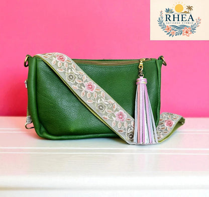 Green handbag with floral strap and tassel on a pink background, featuring the Rhea brand.