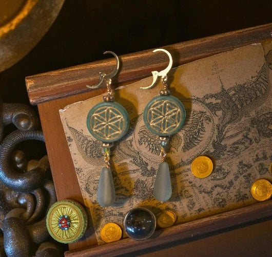 Pair of earrings with green and gold designs on a decorative card.