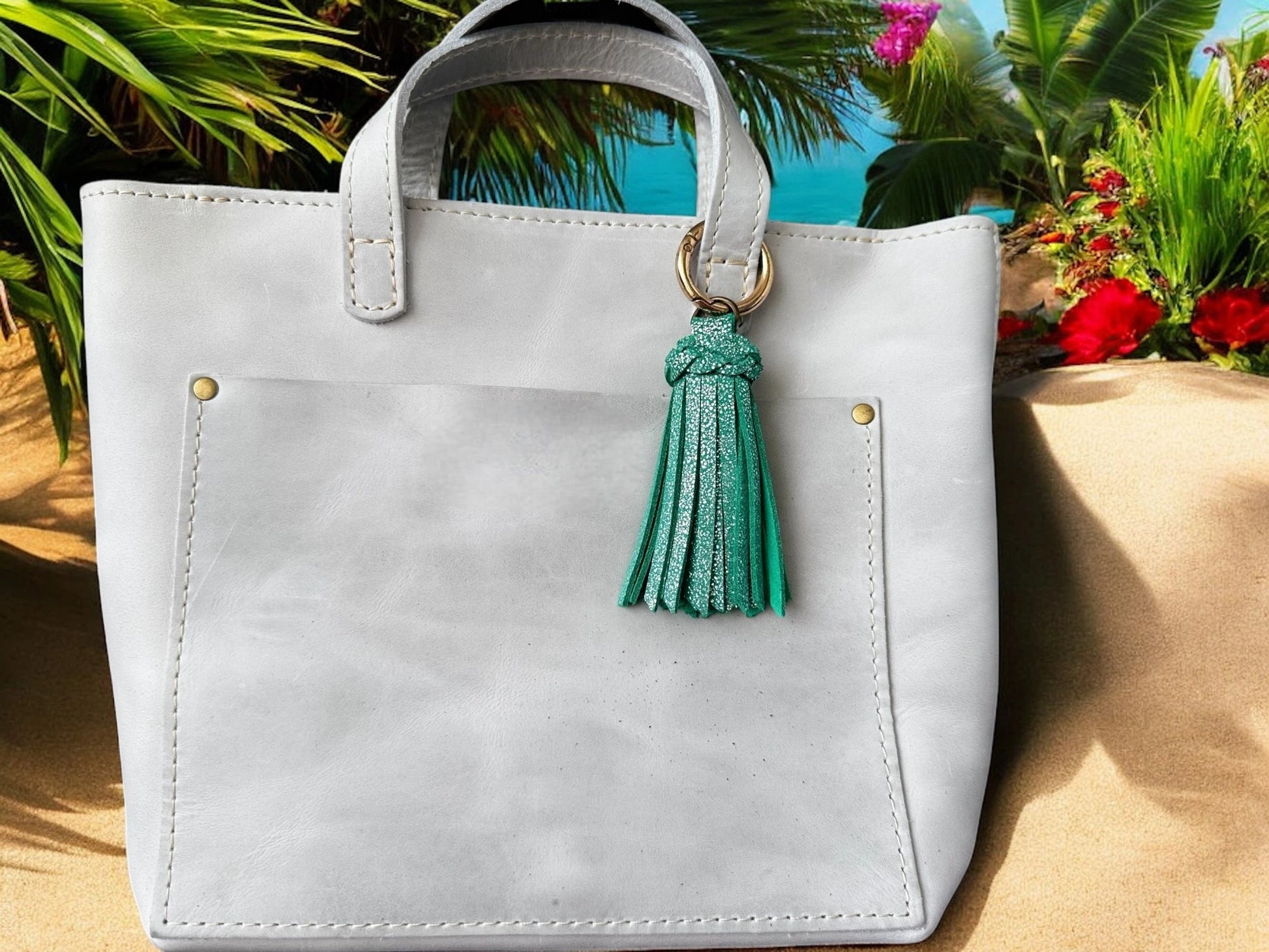 White handbag with a green tassel against a tropical background
