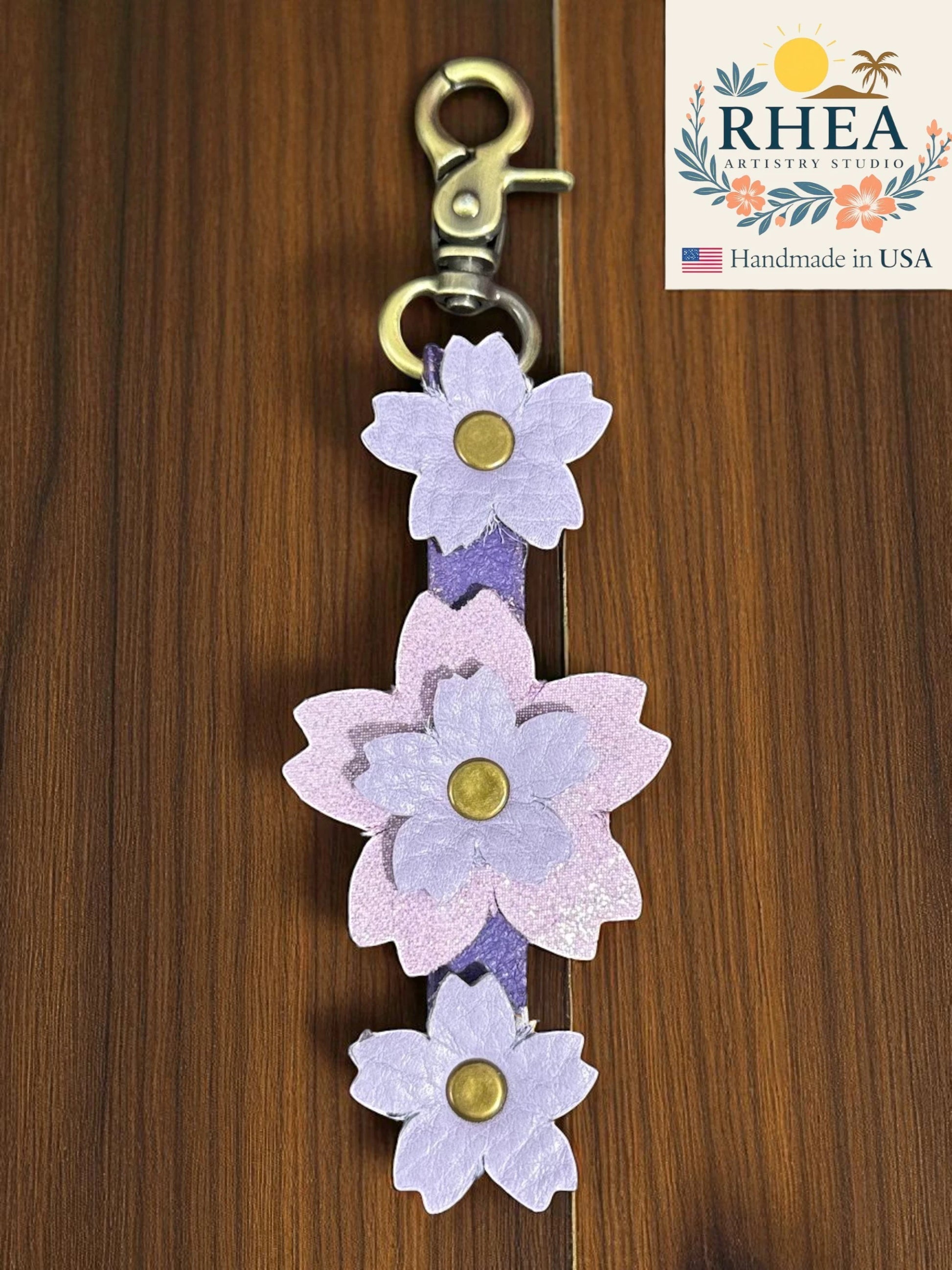 handmade leather bag charm lavender accents on a wooden background, featuring the RHEA Artists Studio logo.