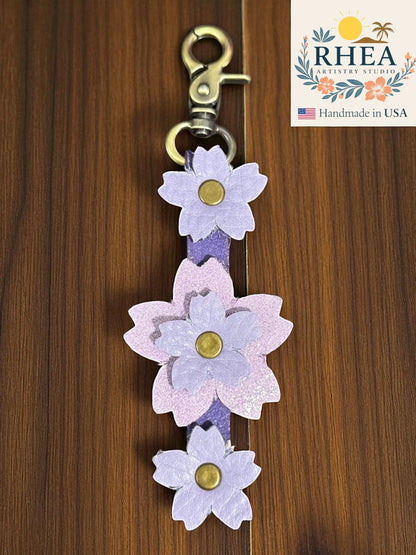 handmade leather bag charm lavender accents on a wooden background, featuring the RHEA Artists Studio logo.