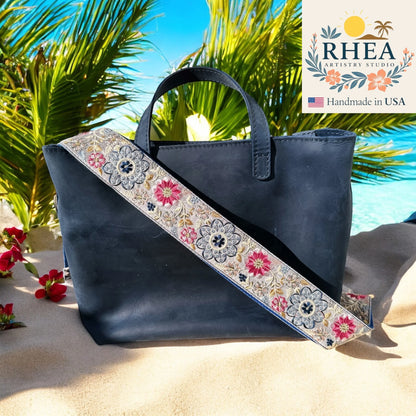 Navy blue handbag with floral purse strap on a beach background, featuring the RHEA Artistry Studio logo.