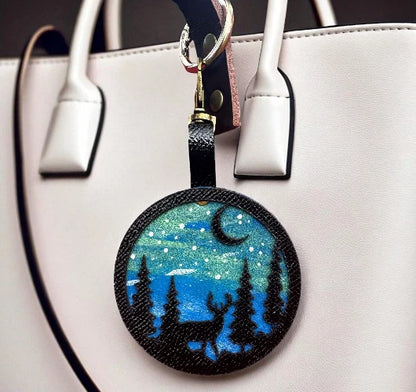 Round keychain with bear and moon design hanging from a white handbag.