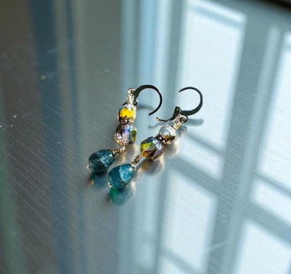 Multicolored beaded earrings on a reflective surface with light and shadow.