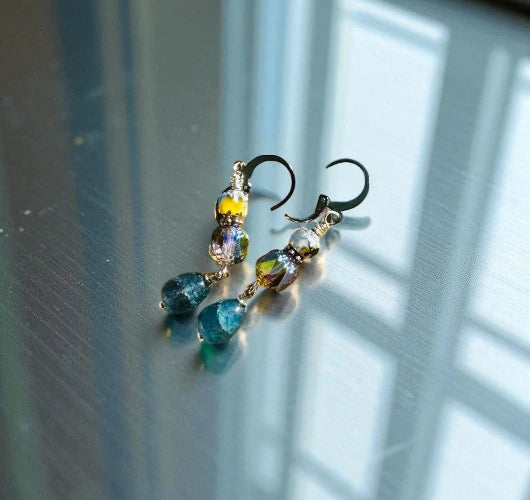 Multicolored beaded earrings on a reflective surface with light and shadow.