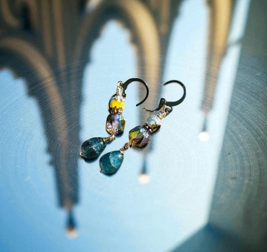 Beaded earrings with colorful stones hanging against a blurred architectural background