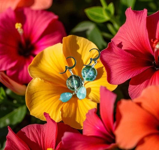 Earrings with green and blue stones on a yellow flower surrounded by pink and red flowers.