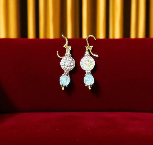 Pair of earrings with gemstones on a red surface with gold curtain background