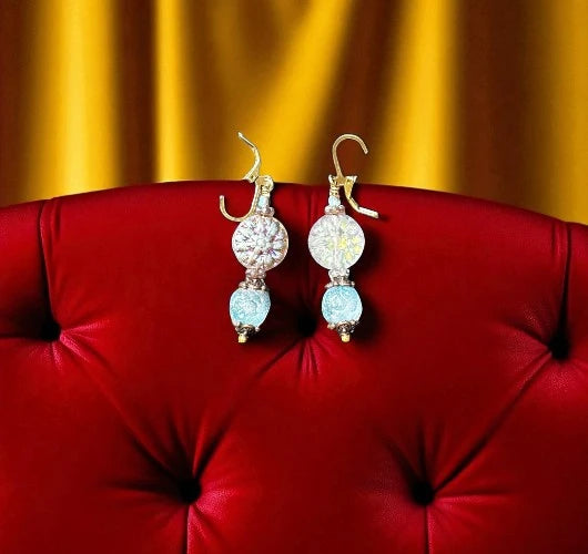 Pair of earrings with blue and clear gemstones on a red surface with a yellow curtain background