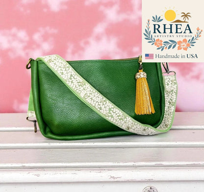 Green handbag with decorative strap and tassel on a pink background, featuring RHEA Artistry Studio logo.