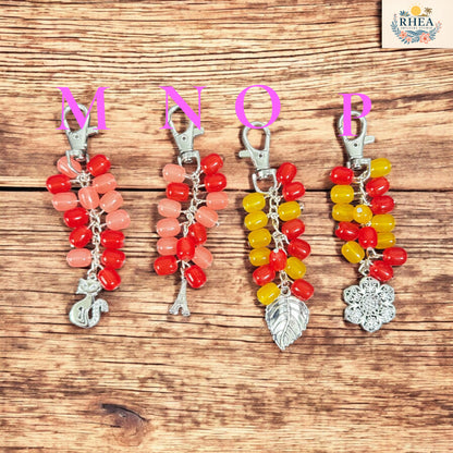 Four colorful keychains with letter charms on a wooden surface, branded 'RHEA'.