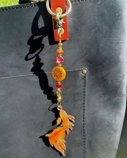 A handcrafted leather charm with a koi fish design, featuring solid brass hardware and high-end designer quality Czech glass, attached to a black leather strand.