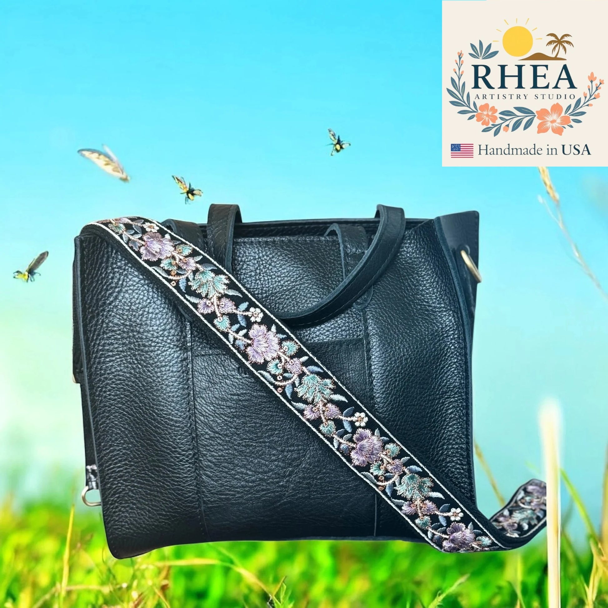 Black leather handbag with floral strap against a natural background, featuring the RHEA Artistry Studio logo.