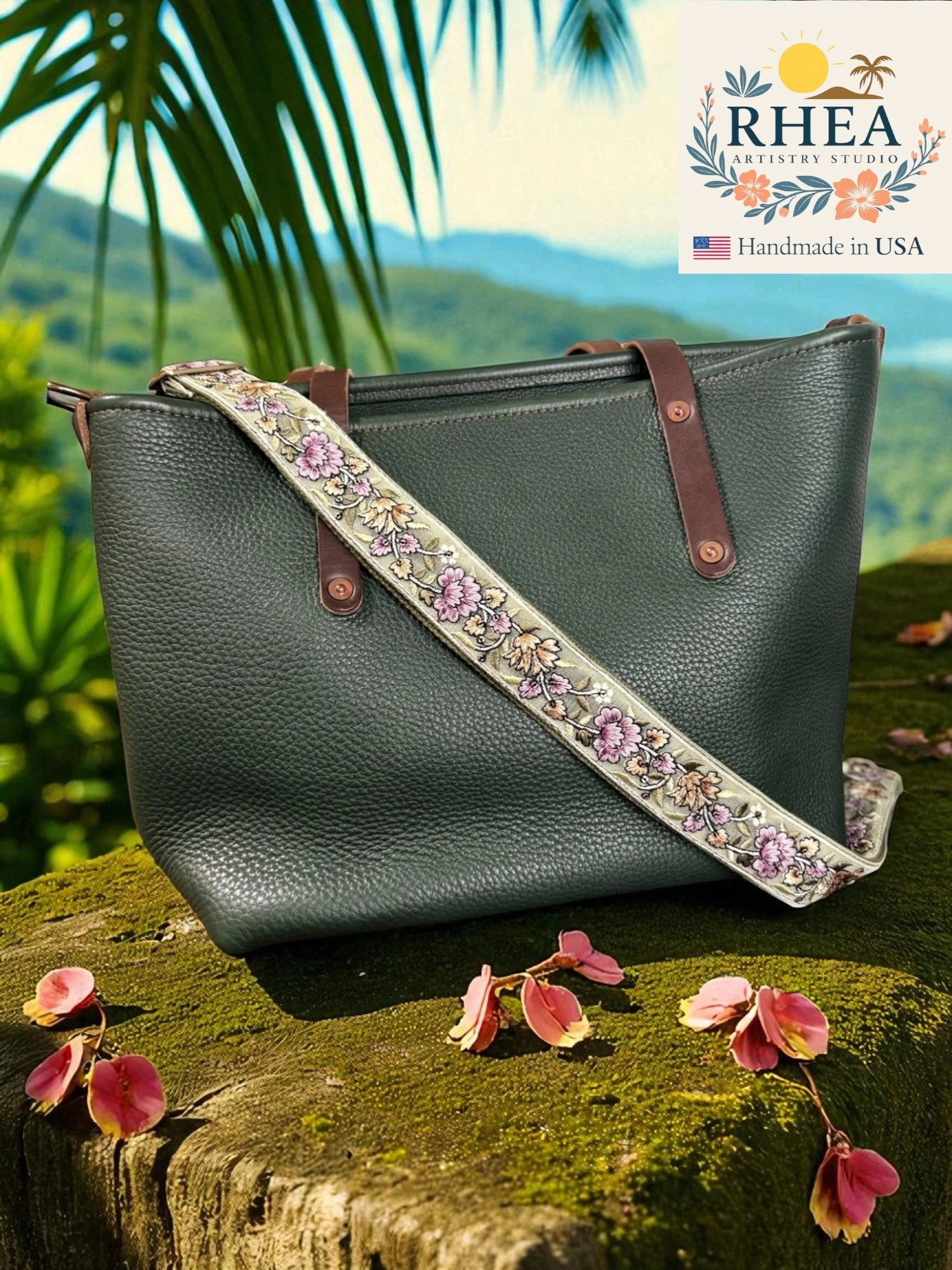 Green leather handbag with floral strap on a stone surface with a scenic background, featuring the RHEA brand.