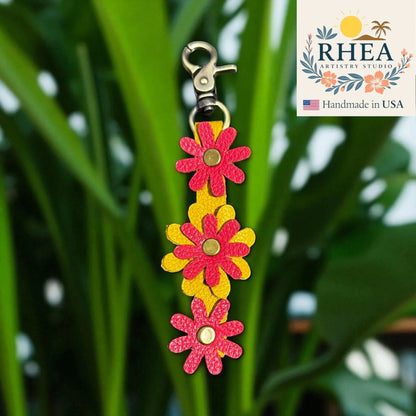 Floral leather purse charm with RHEA Artistry Studio branding on a green leaf background