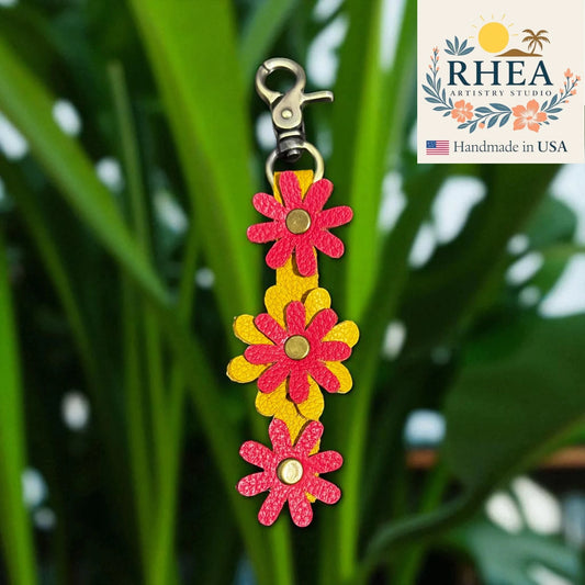 Floral leather purse charm with RHEA Artistry Studio branding on a green leaf background