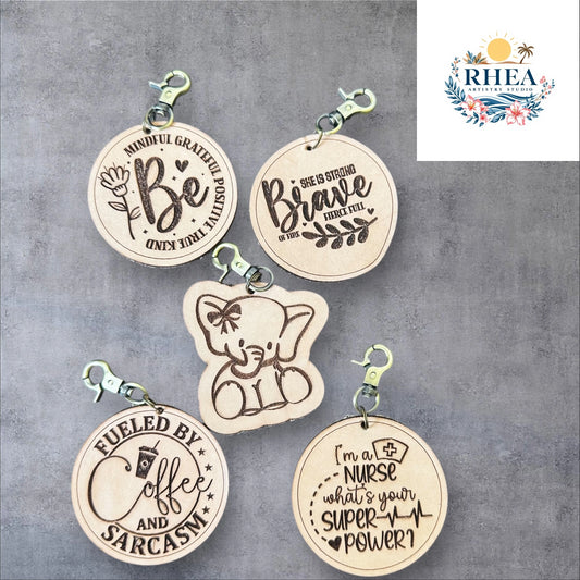 Five wooden keychains with engraved text on a gray background, featuring the brand 'RHEA'.