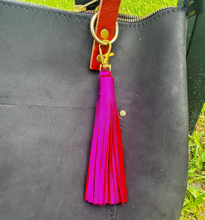 A jumbo leather tassel accessory in hot pink color, displayed on a black handbag with a red strap.