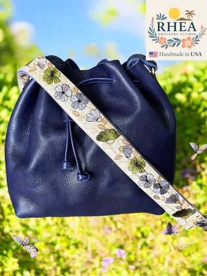 Navy blue leather bag with floral purse strap against a blurred natural background
