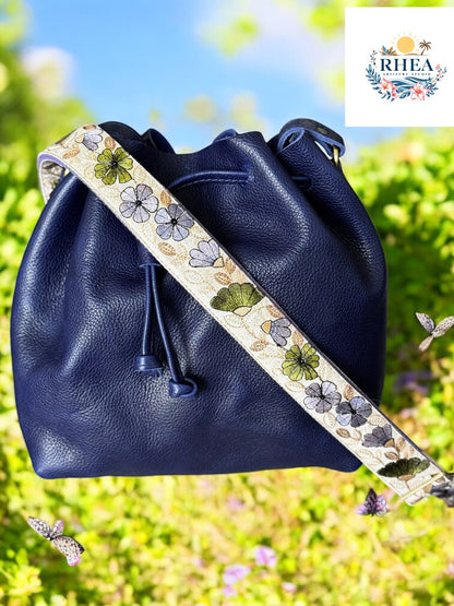 Navy leather bucket bag with a cream strap detailed in violet, sage, and charcoal floral motifs.