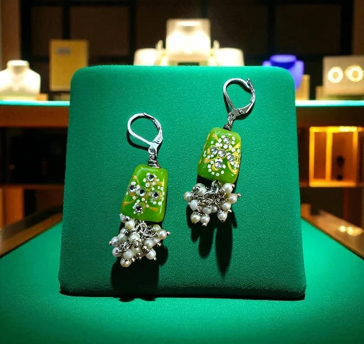 Green earrings with pearl and gemstone details on a green stand.