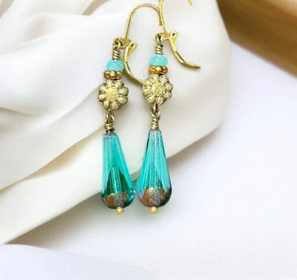 Handmade turquoise glass drop earrings with gold floral charms and aqua bead accents, displayed on white fabric.