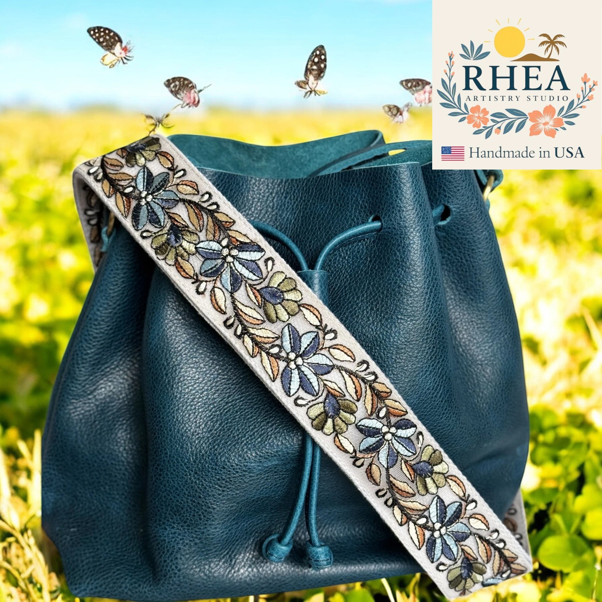 Blue leather bag with an embroidered purse strap featuring butterflies, set against a blurred natural background.