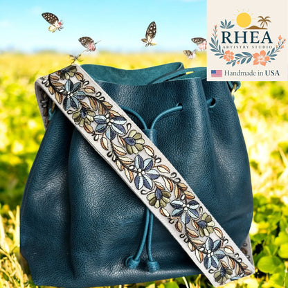 Blue leather bag with an embroidered purse strap featuring butterflies, set against a blurred natural background.