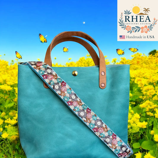 Turquoise tote bag with floral purse strap in a field of yellow flowers, featuring RHEA Artistry Studio logo.
