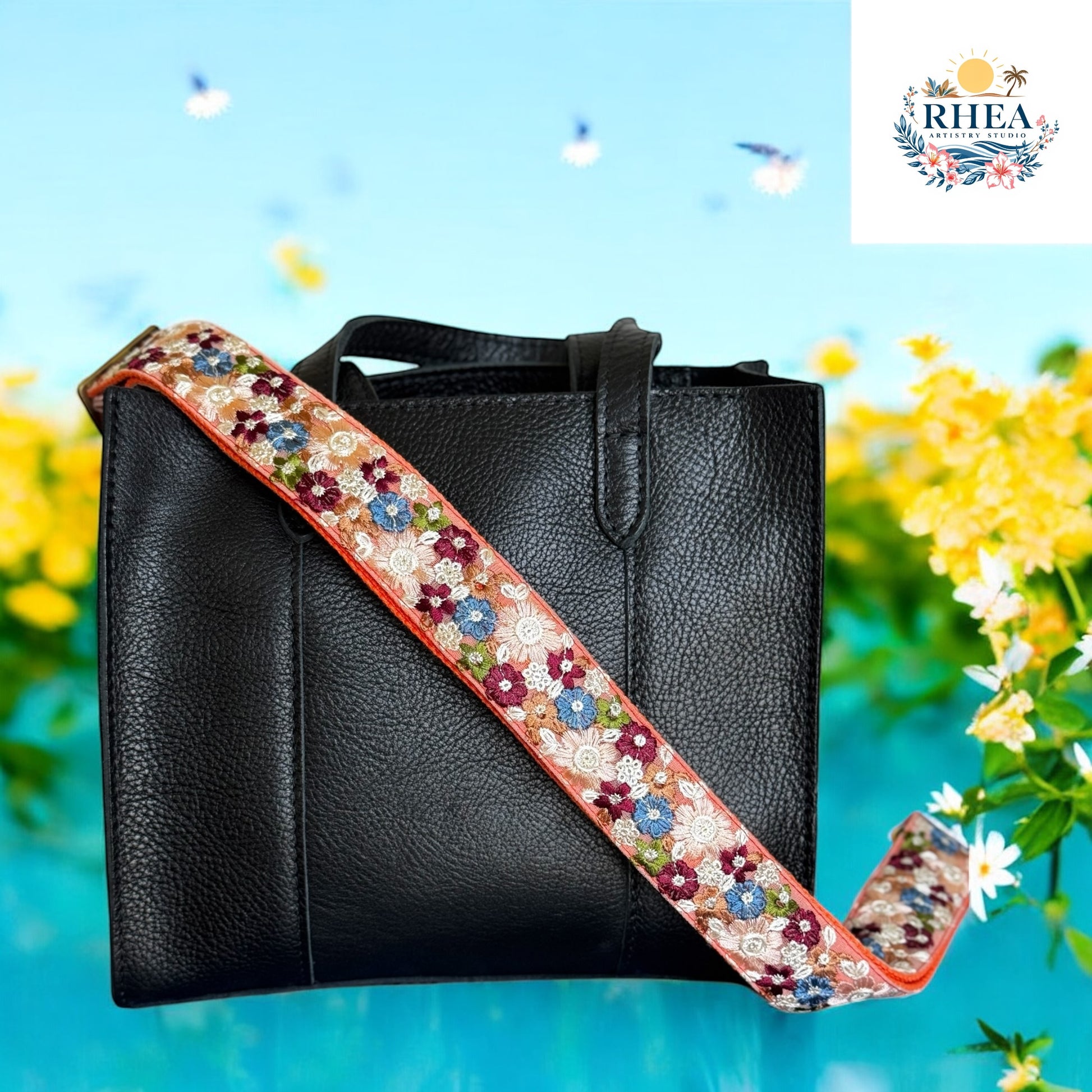  Black leather handbag with a coral strap embroidered in burgundy, blue, ivory, and green floral designs, set against a wildflower garden backdrop.