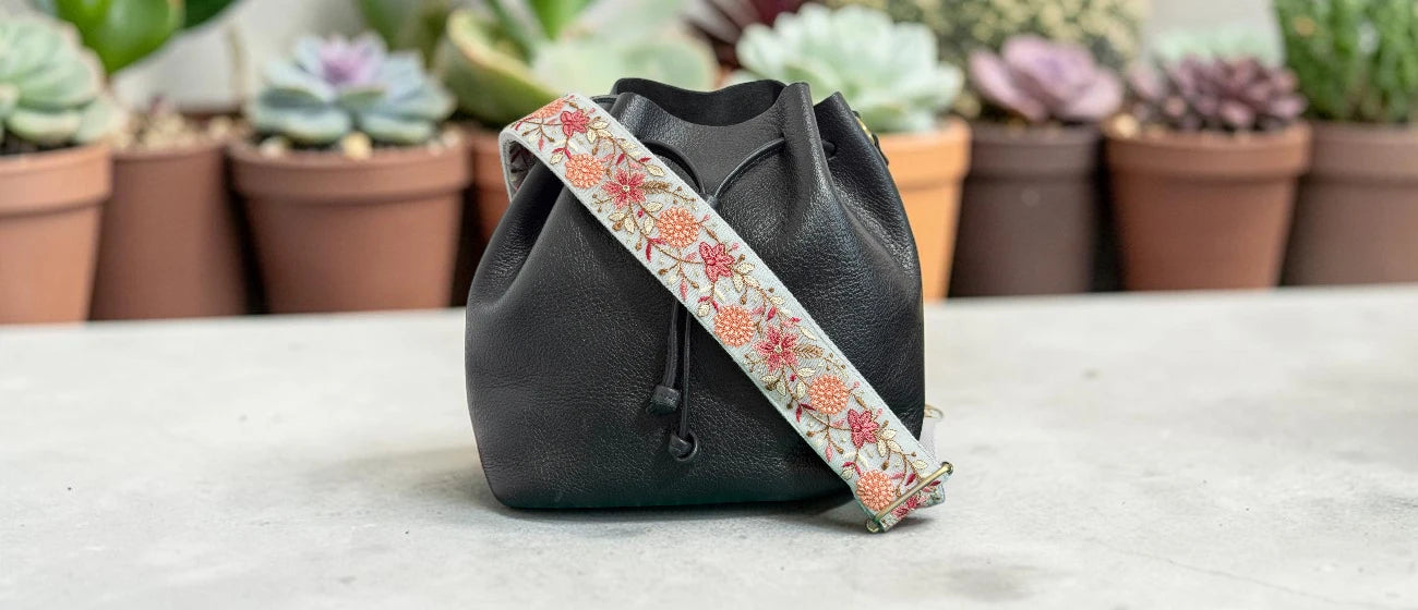 Black drawstring bag with a floral strap on a light surface with plants in the background
