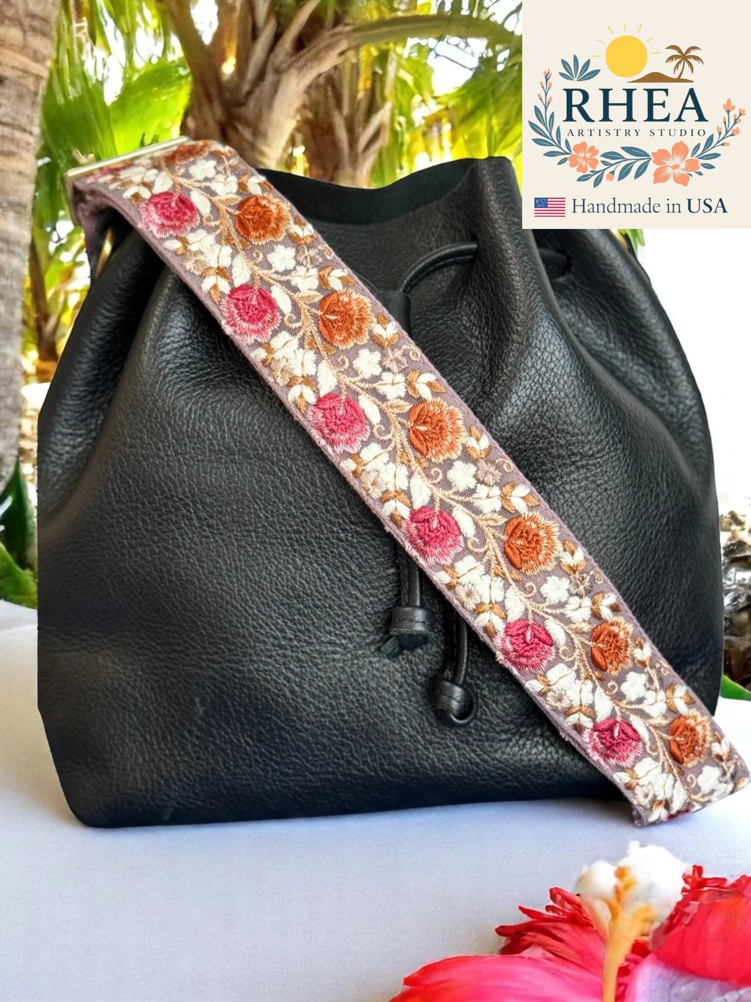 Black leather bag with a decorative floral purse strap, RHEA brand logo visible.
