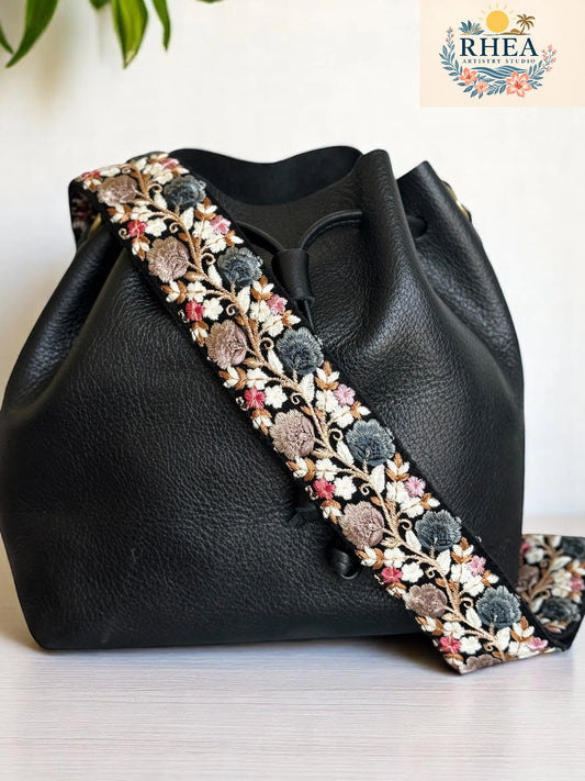 2-inch wide artisan strap with dusty pink, blue, and beige florals embroidered on black, styled on a black leather bag.