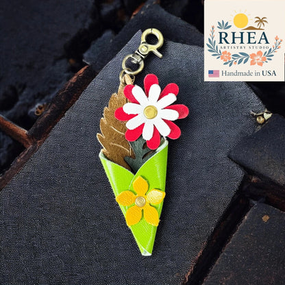 Floral-themed leather boquest charm with 'RHEA' branding on a dark textured background