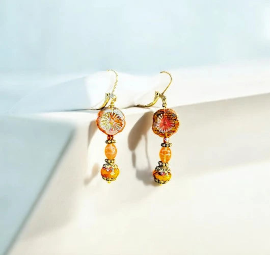 Pair of mustard and gold beaded earrings on a white stand with a light blue background