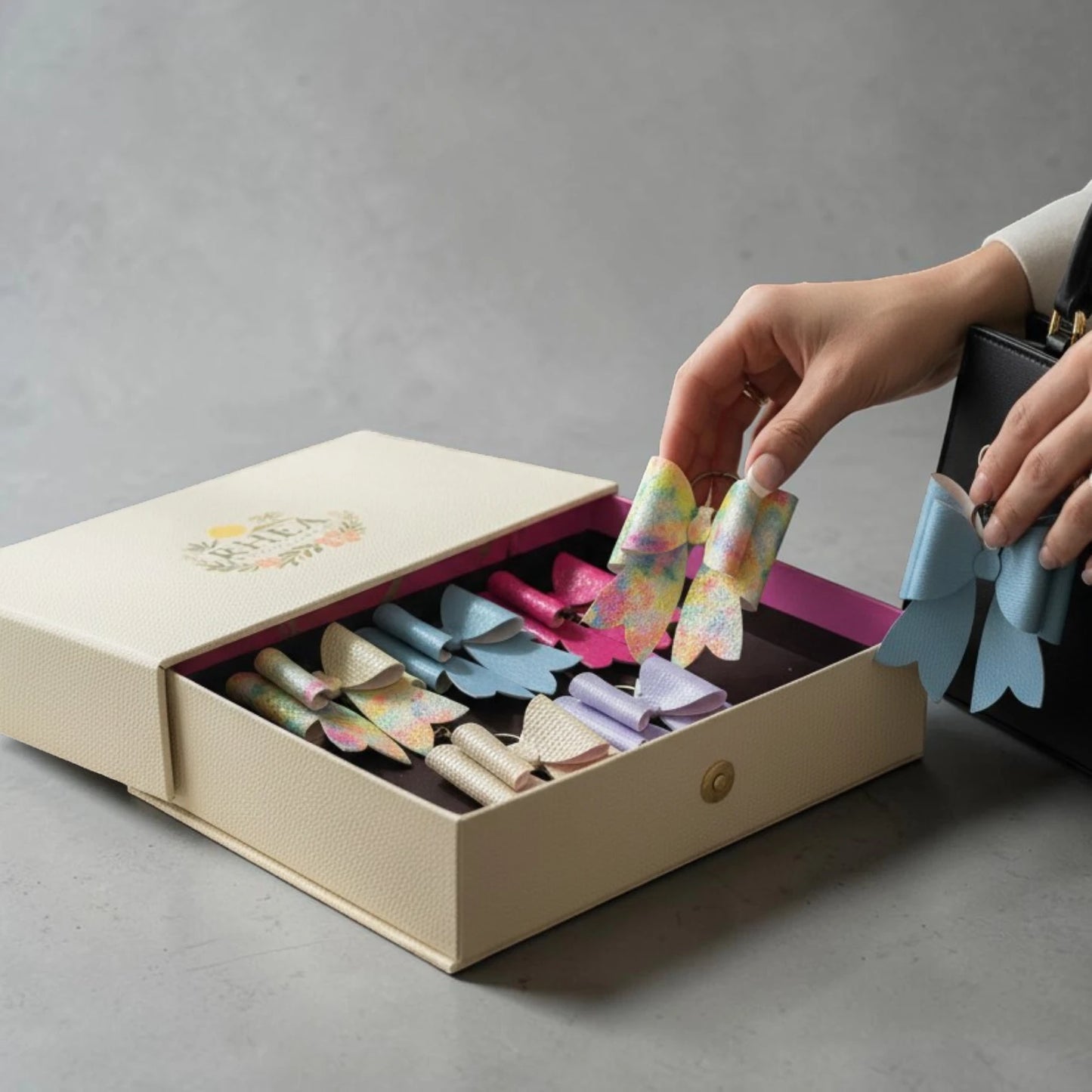 Grand Surprise mystery bow charm set with assorted handmade bow charms in a gift box and one bow clipped to a handbag