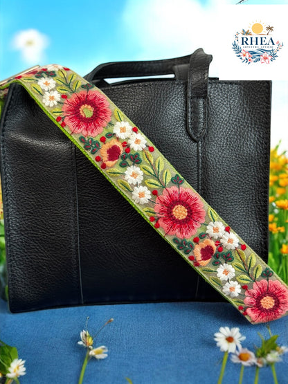 Olive green floral crossbody strap with crimson daisies and ivory blossoms attached to a structured black leather handbag.