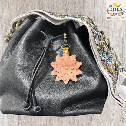 Black leather drawstring bag with a floral keychain on a wooden surface, Handmade leather flower accessory designed to elevate everyday bags